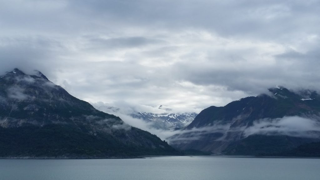 A panoramic views of a bay surrounded by tall misty and snowy mountains. 