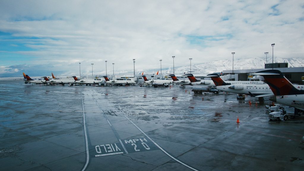 Aircrafts parked by a runway with markings "yield" and "20 mph" at an airport in the mountains.