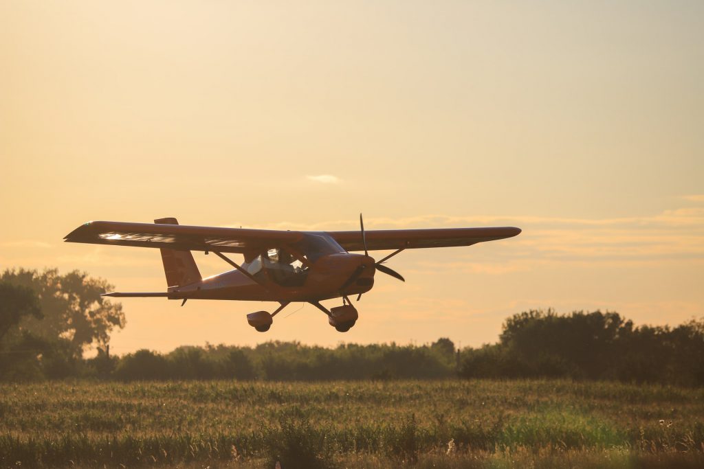 A bush pilot flying a small personal airplane low over a field of crops.