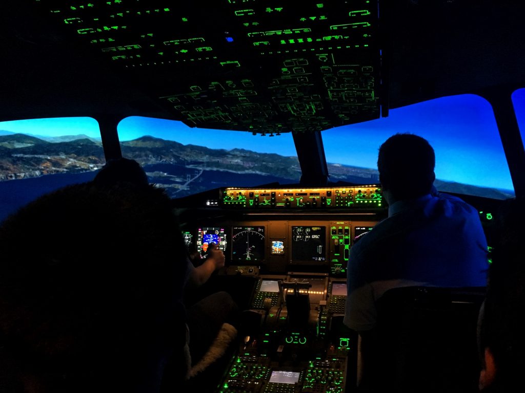 Two pilots sitting in a cockpit of a plane, which is flying over a bay in a mountain region.