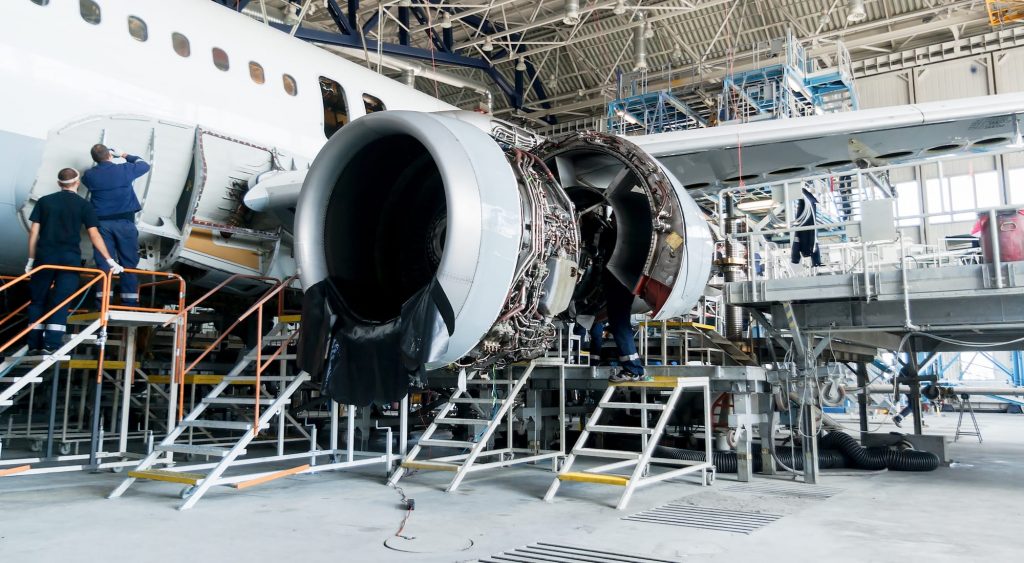 Aircraft engineers disassembling and working on an aircraft jet engine at an MRO facility.