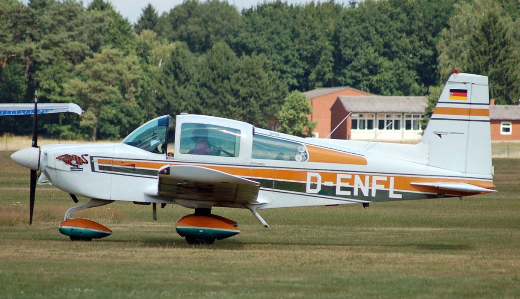 Grumman Tiger AA 5B aircraft with its pilot standing at an airfield in Germany. 