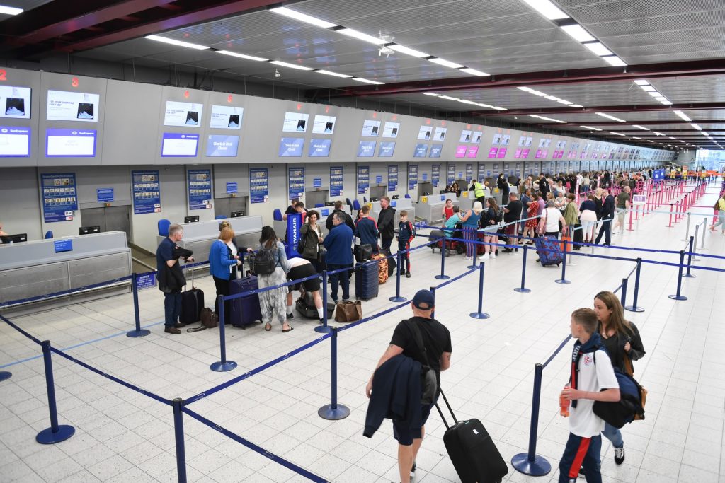 An airport terminal with information management systems and many travellers using them. 