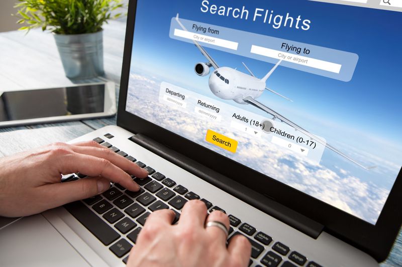 A person sitting at a desk with a laptop, booking flight tickets online. 