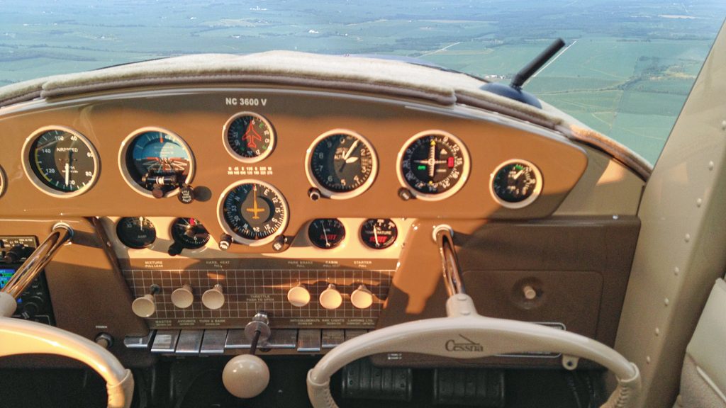 A Cessna 140 aircraft cockpit, instrument panel, and control columns in sunlight.