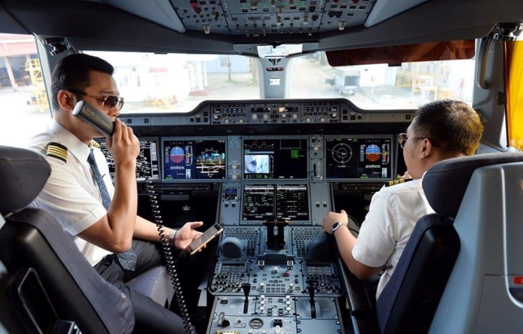 A backview of two pilots sitting inside the cockpit of an airplane, working on the instrument panel.