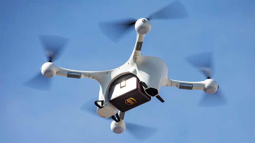 A view of a small UPS cargo drone with a box attached to it in flight. 