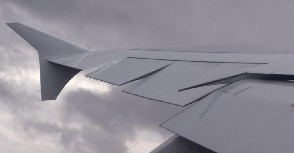 Flight spoilers on an aircraft wing during flight in a cloudy sky.