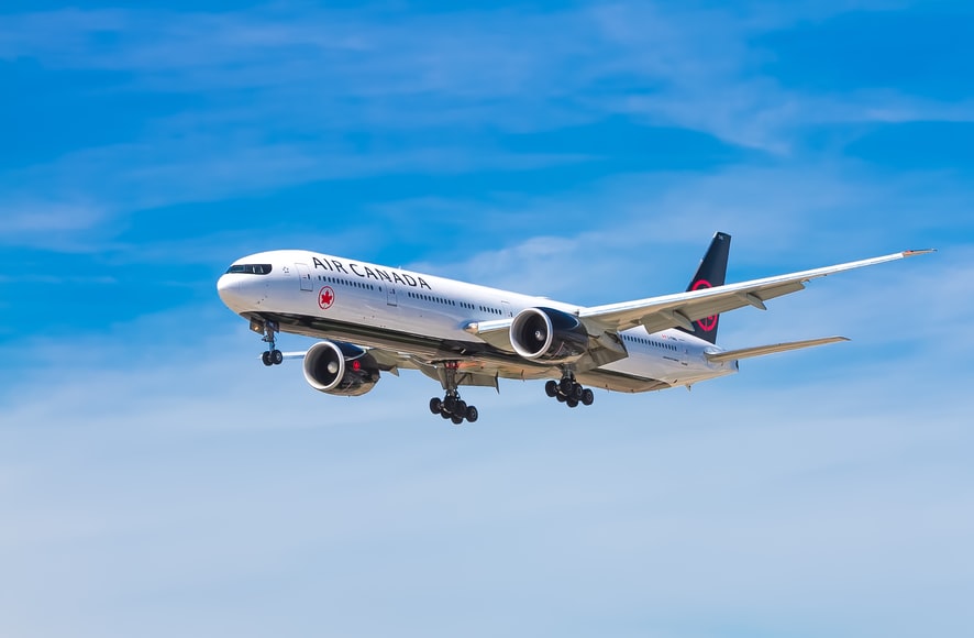 An Air Canada Boeing 777 in flight across a blue sky, ready to land. 