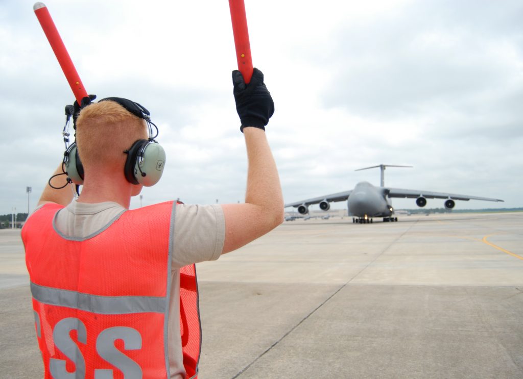 Maintenance team marshal is signaling a C-5 aircraft for takeoff at a military airbase.