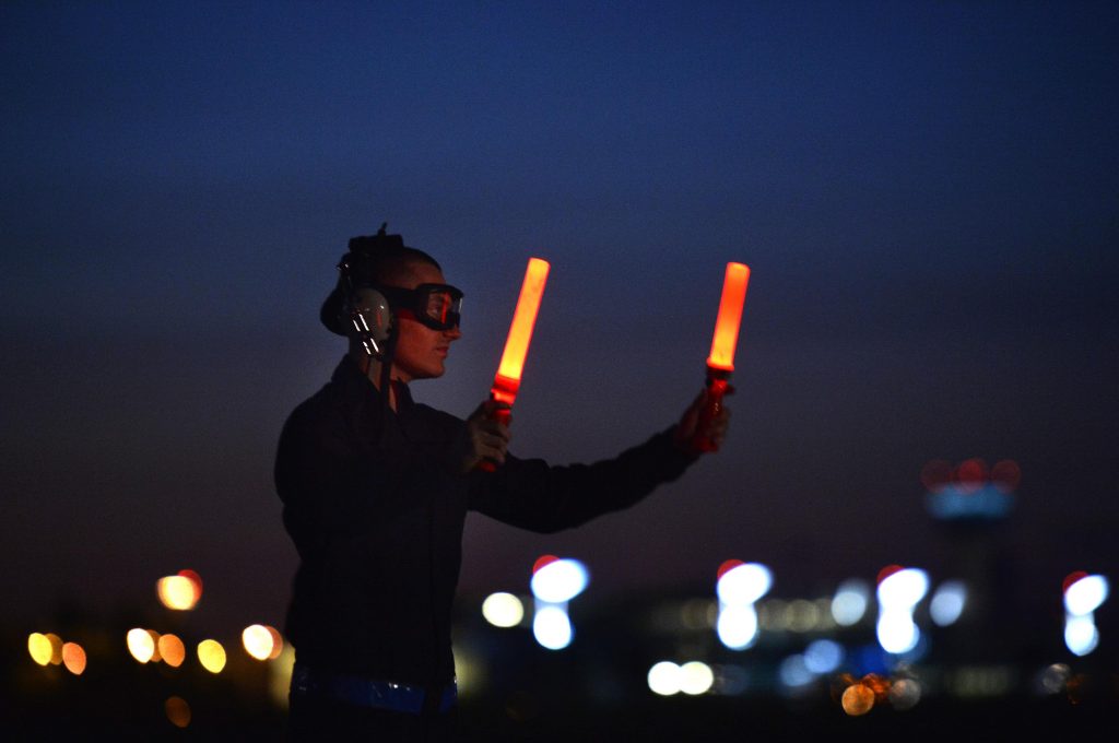 An aircraft marshal with protective gear and air marshalling wands is directing and aircraft. 