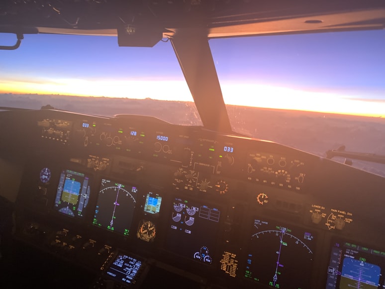 A commercial airlines aircraft flying above clouds at sunset.