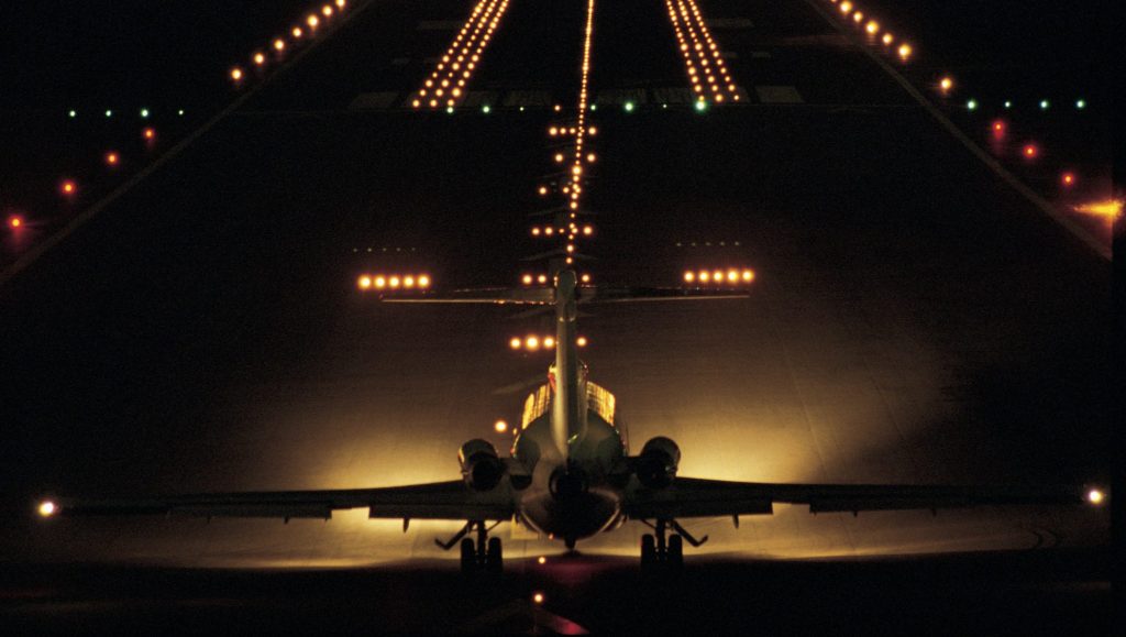 A commercial aircraft with lights on an illuminated runway at night. 
