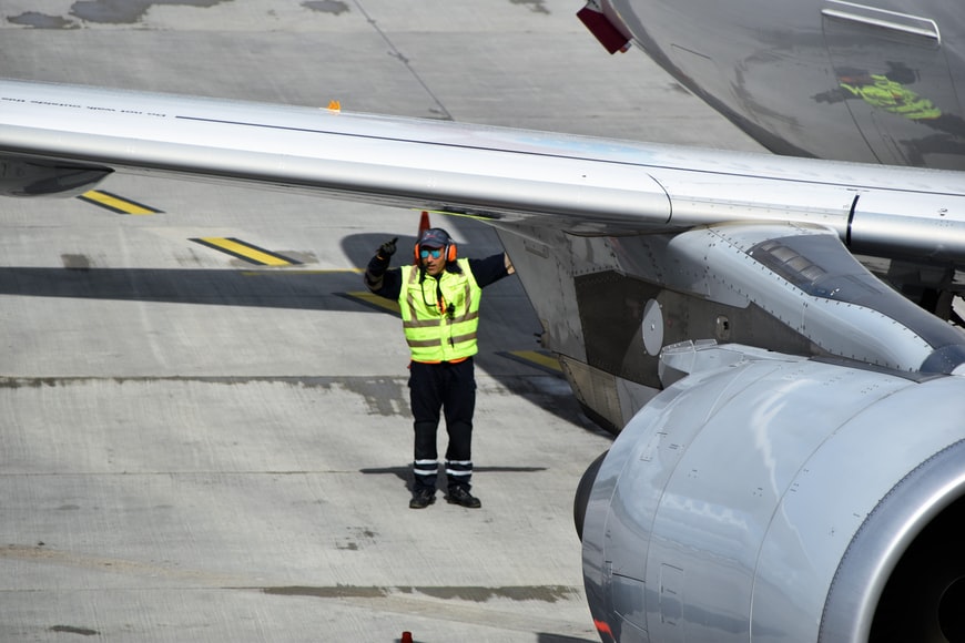 An airport worker wearing protective head gear and a reflective yellow vest, as it is required by safety management systems.