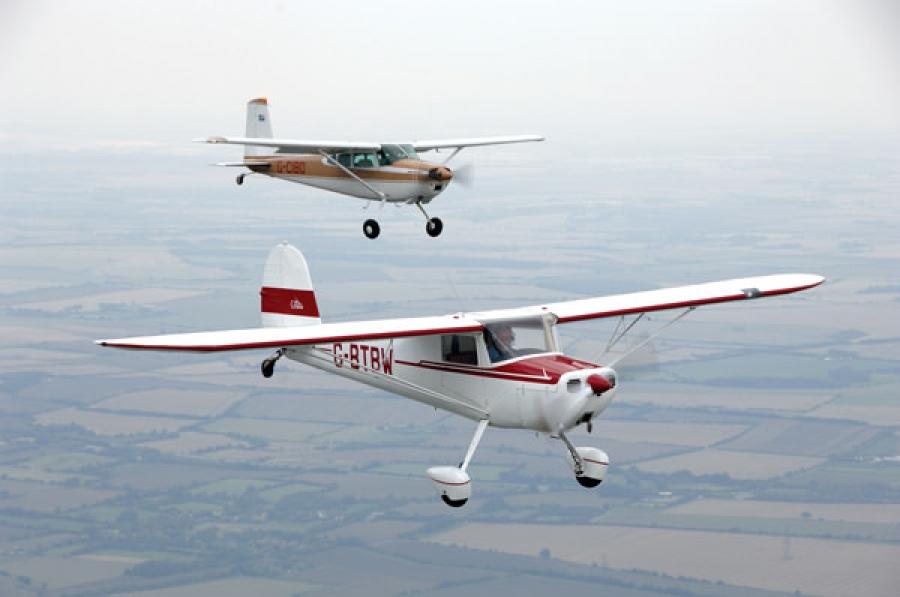 Two Cessna 120 type aircrafts flying over farm fields.
