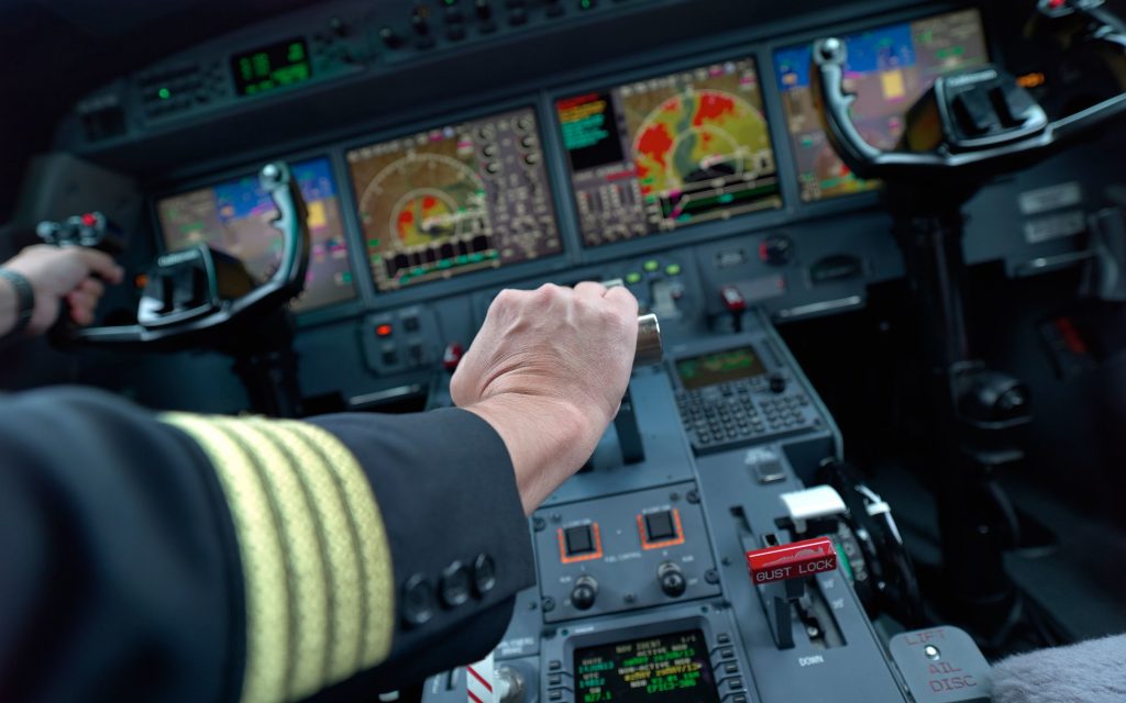 An aircraft captain in a cockpit navigating a plane, sitting at the instrument panel. 
