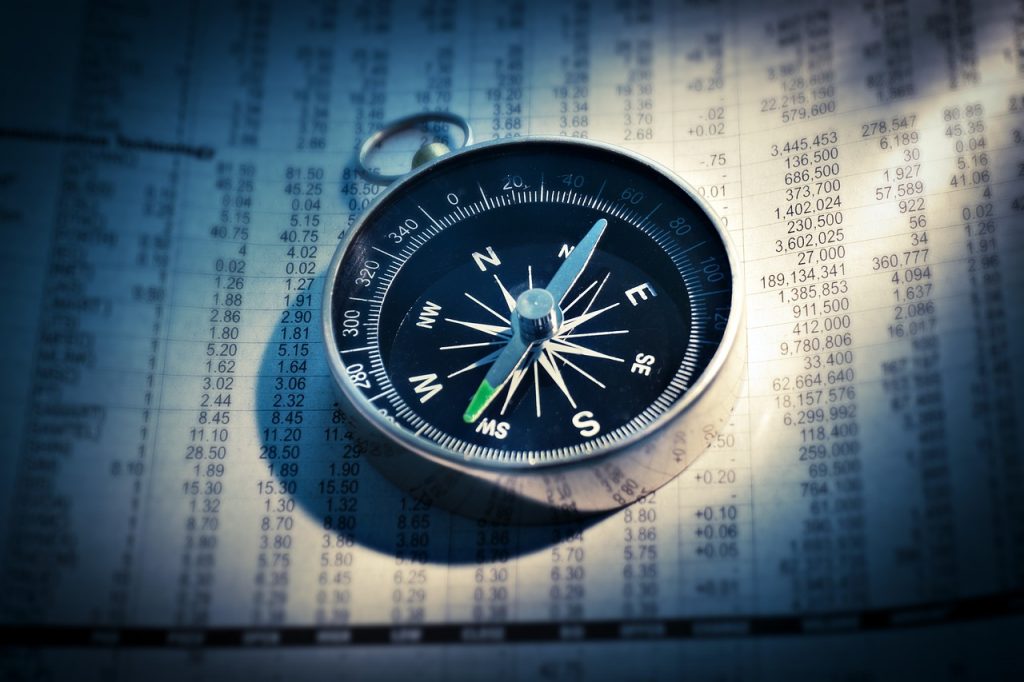 A central view of a compass indicating a clear direction to south west laying on a sheet of paper with many numbers.