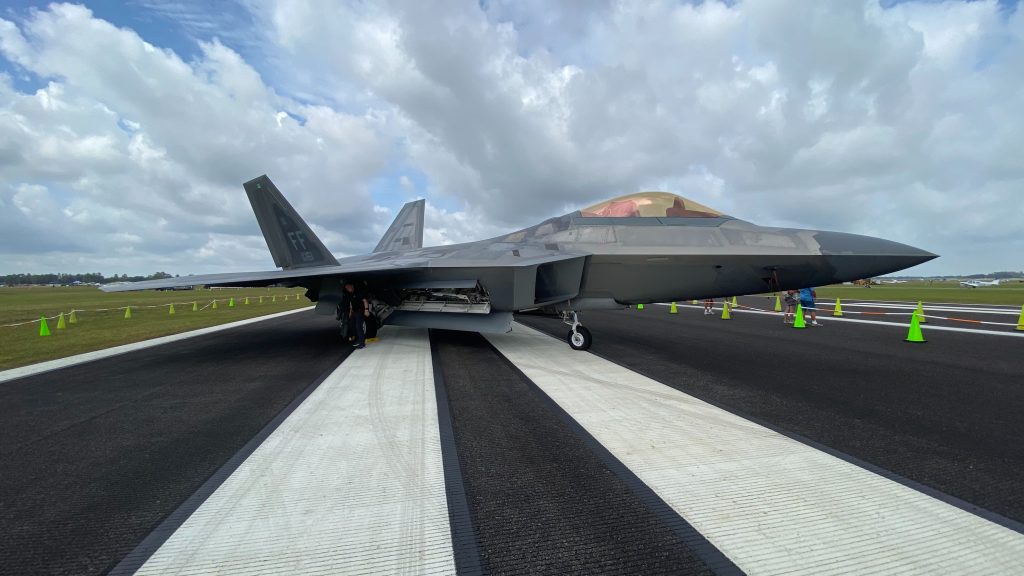 A fighter jet F-22 Raptor parked on a runway of an airfield at daytime.