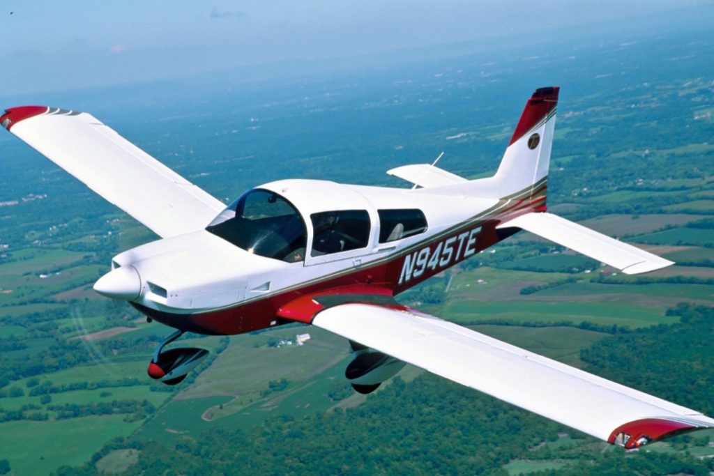 A Grumman Tiger aircraft in flight over fields and forests.