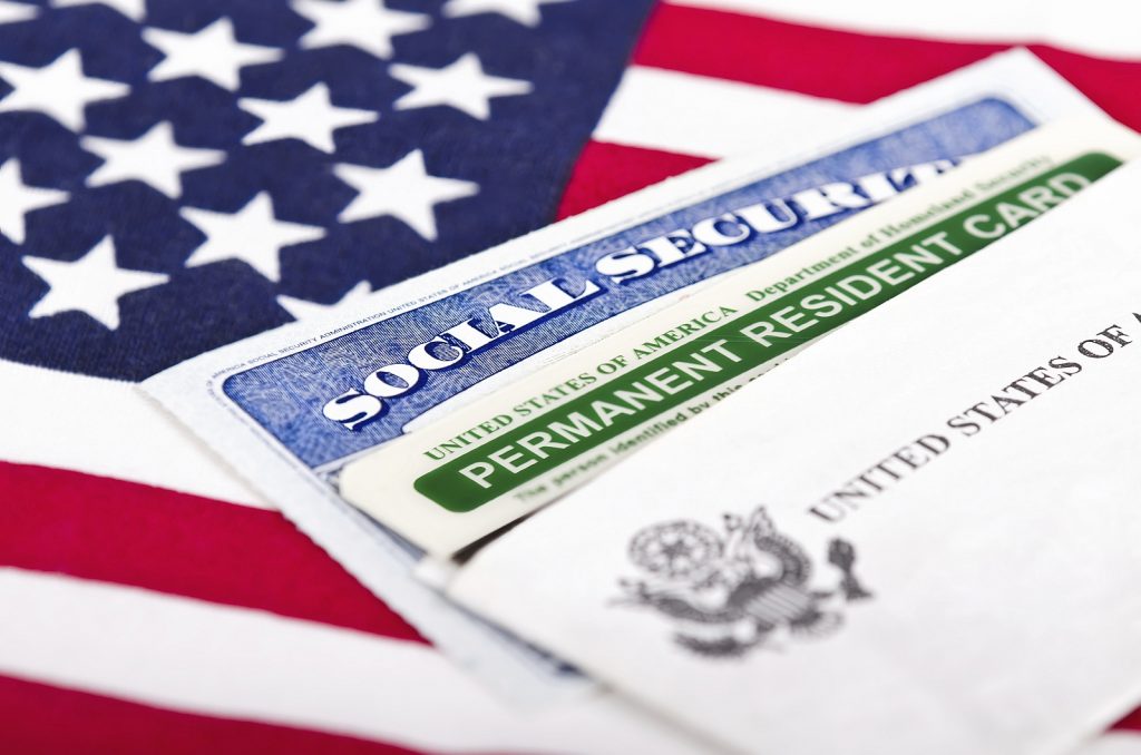 A green card, a social security card and the flag of the USA from a central view.