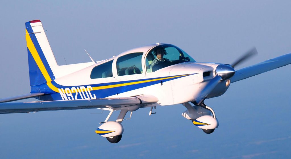 A central view of Grumman Tiger AA 5B aircraft in blue, flying high above ground. 