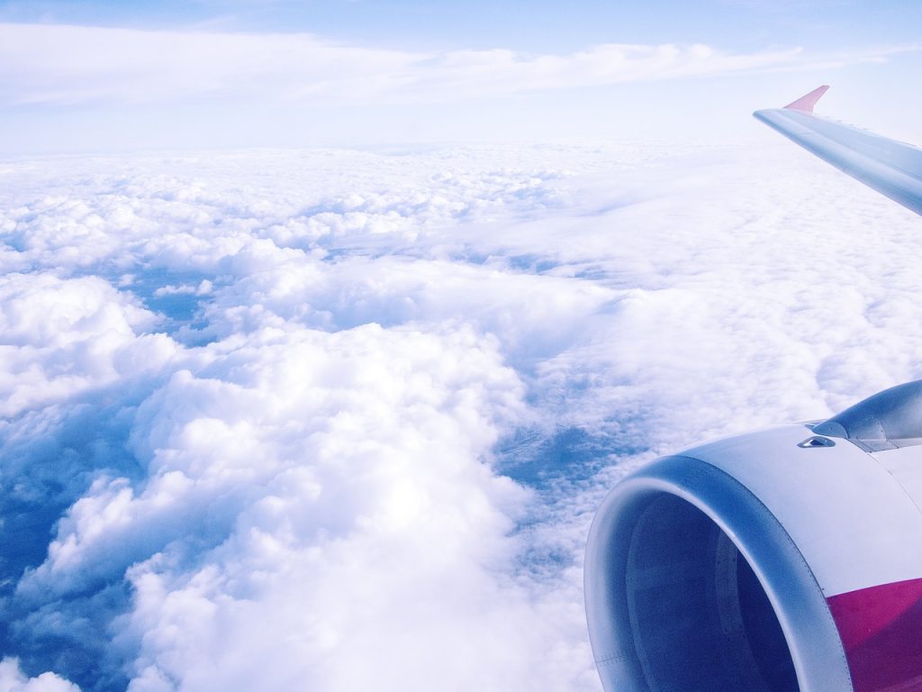 A view from an airplane window of the aircraft wing and the engine while flying high above clouds.