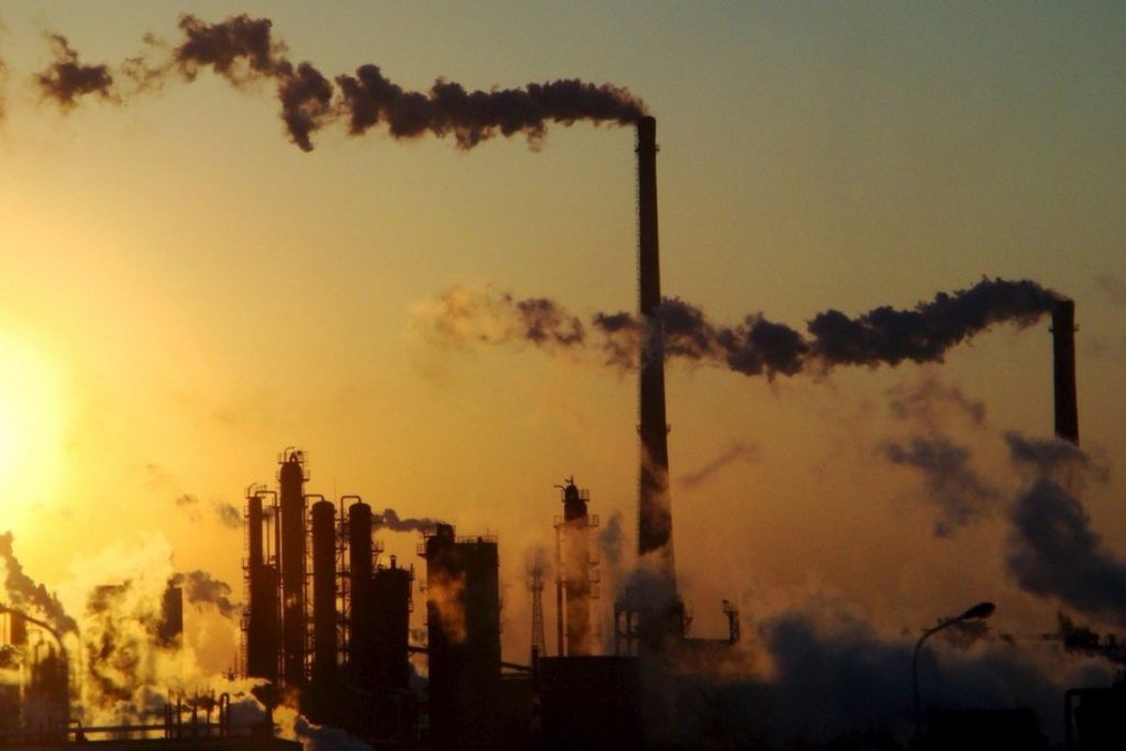 Visible industrial pollution as smoke from a factory and factory chimneys during sunset. 