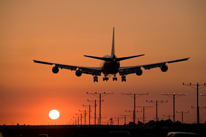 A passenger aircraft landing at an airport runway while the sun is setting. 