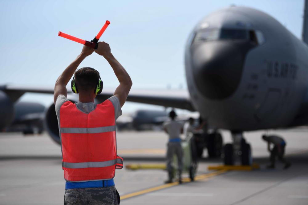 An aircraft marshal signaling a large military aircraft at a military airbase.