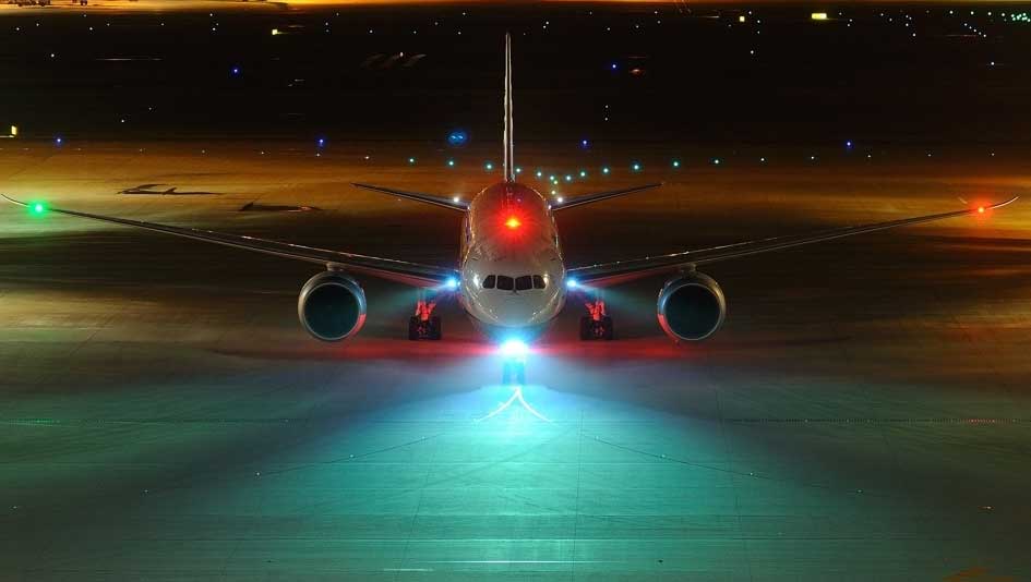 A central view of an aircraft on a taxiway with navigation lights on at night. 
