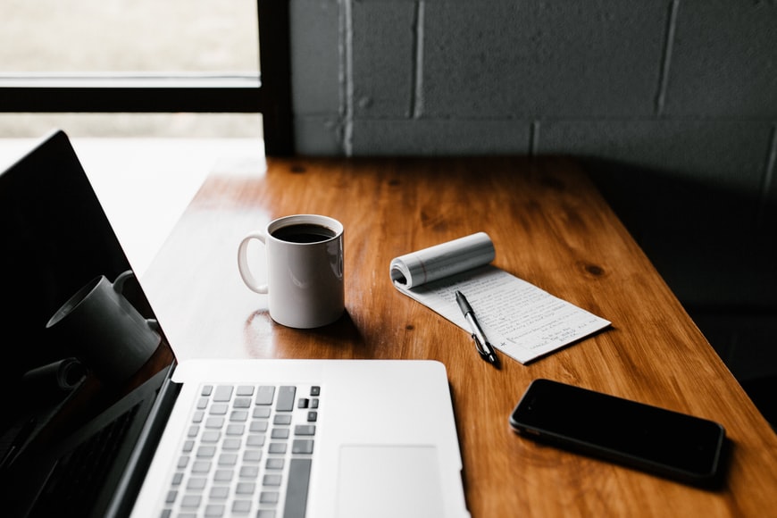 A desk with a laptop, a coffee mug, a notebook and a mobile phone, preparing to do learning in aviation.