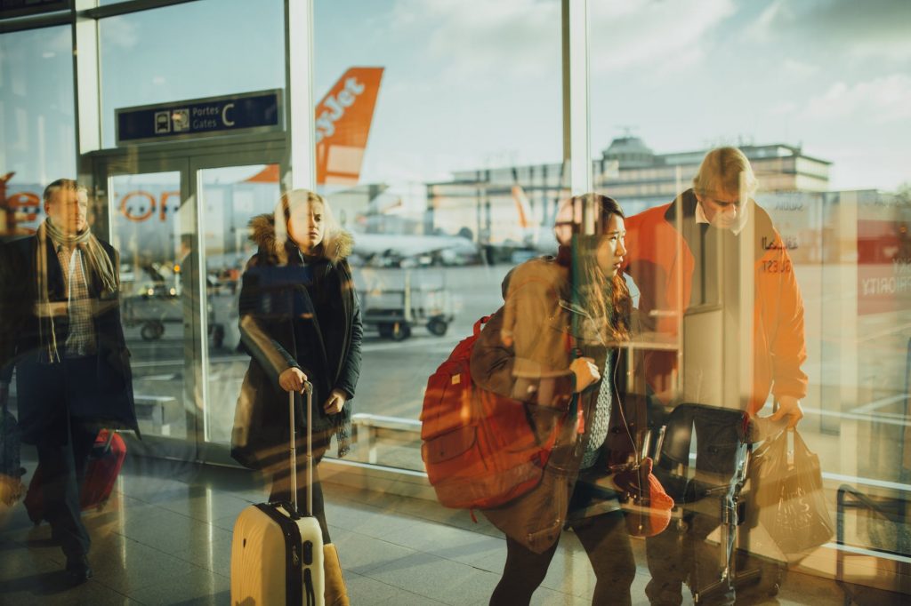 Travelers walking down a corridor of an airport terminal on a sunny day. 