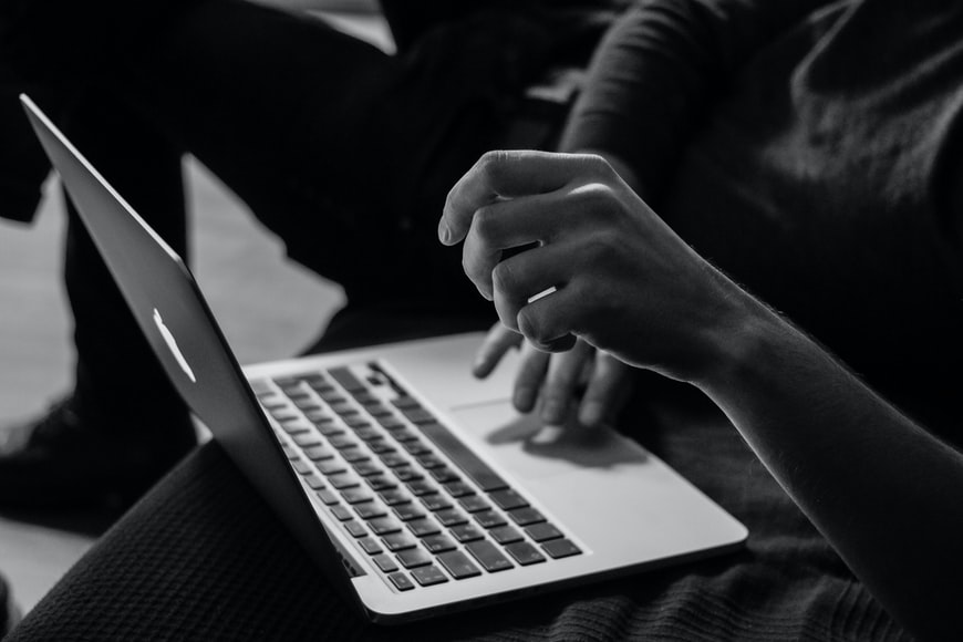 A black and white view of a person sitting in a chair using a piece of technology, a MacBook laptop.