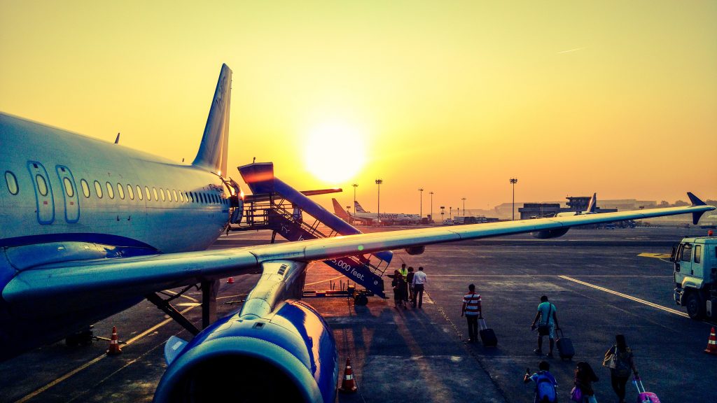 An aircraft is stationed by a taxiway at an airport airfield, passengers are walking towards a boarding platform to get onto the plane.