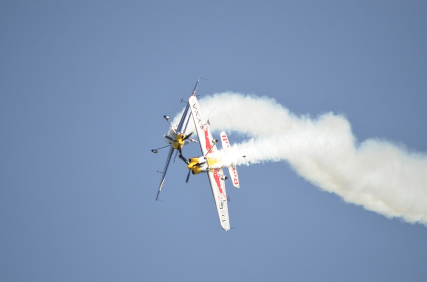 Two small stunt airplanes performing a spiraling maneuver in the sky. 