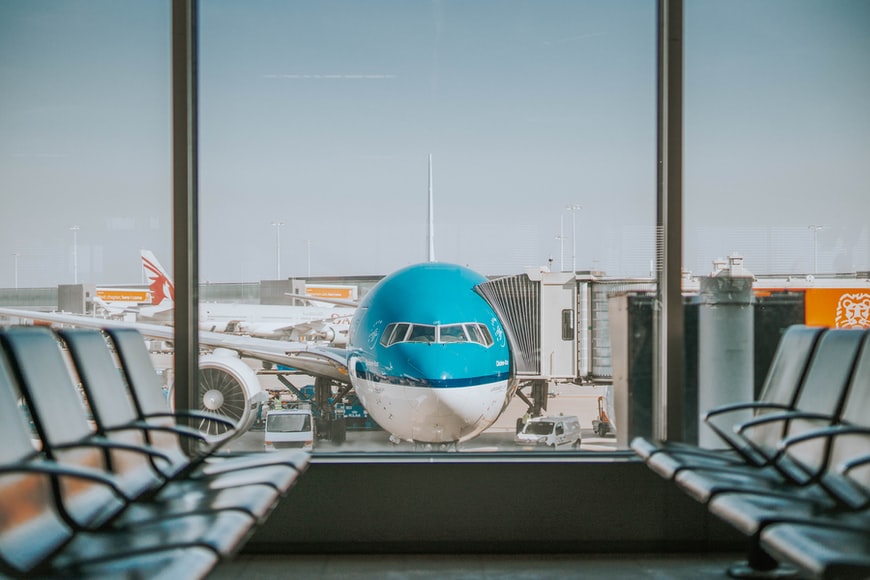 A central view of a waiting hall with windows and a white and blue aircraft connected to a jet bridge.