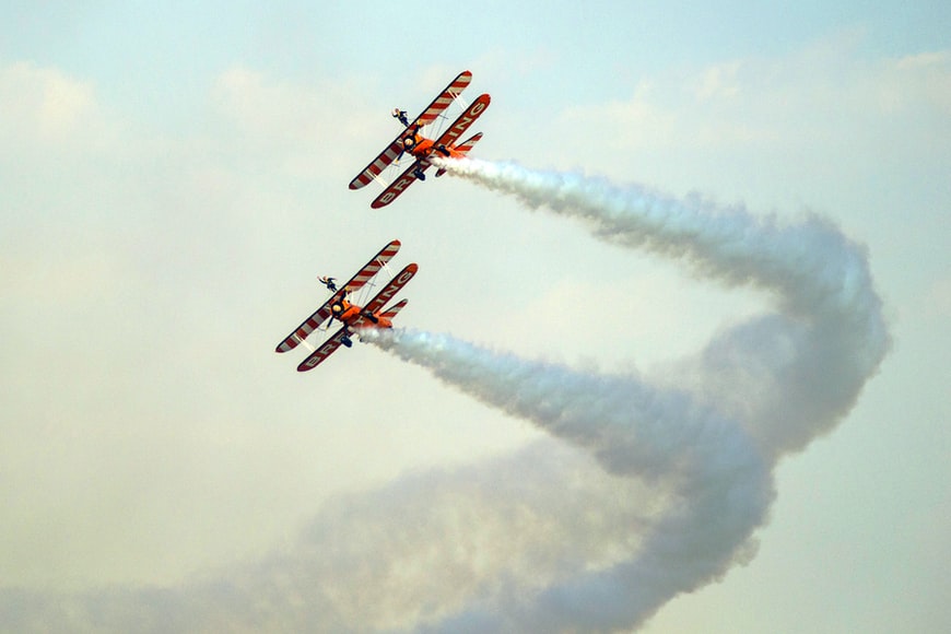 Two orange stunt airplanes performing a stunt in the air. 