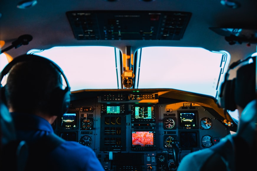 Commercial airline pilots sitting in a cockpit with headphones, flying an aircraft.