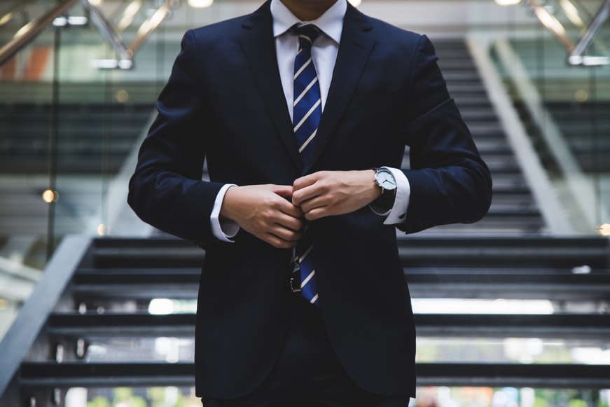 A central view of an aviation professional wearing a dark suit, a striped tie and a watch, standing on stairs.