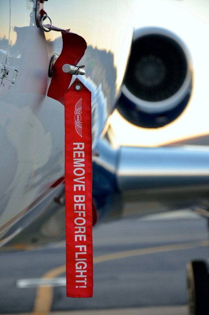 A view of a side of an aircraft and its jet engine, marked with a tag "remove before flight".