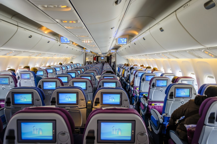 A pressurized aircraft cabin with passengers sitting in seats equipped with screens. 