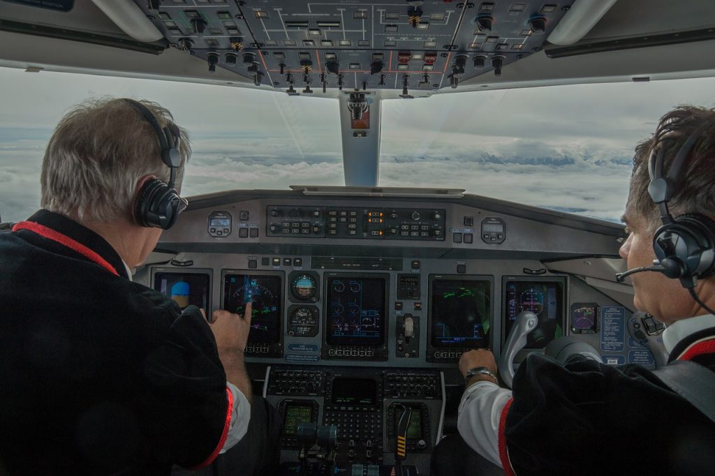 Two airline pilots in uniform in a cockpit of an aircraft flying high above heavy gray clouds. 