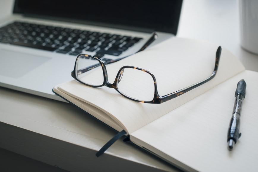 A desk of a person, who is ready to participate in distance learning courses, with glasses, notebook, and a pen prepared.