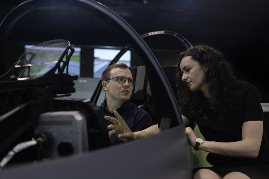 A young flight school student is being instructed by a female instructor on how to operate an aircraft in flight simulator.