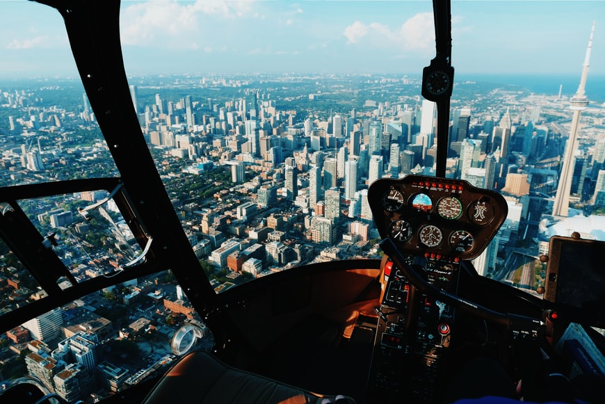 An image of a helicopter cockpit, navigating over skyscrapers in a large city.