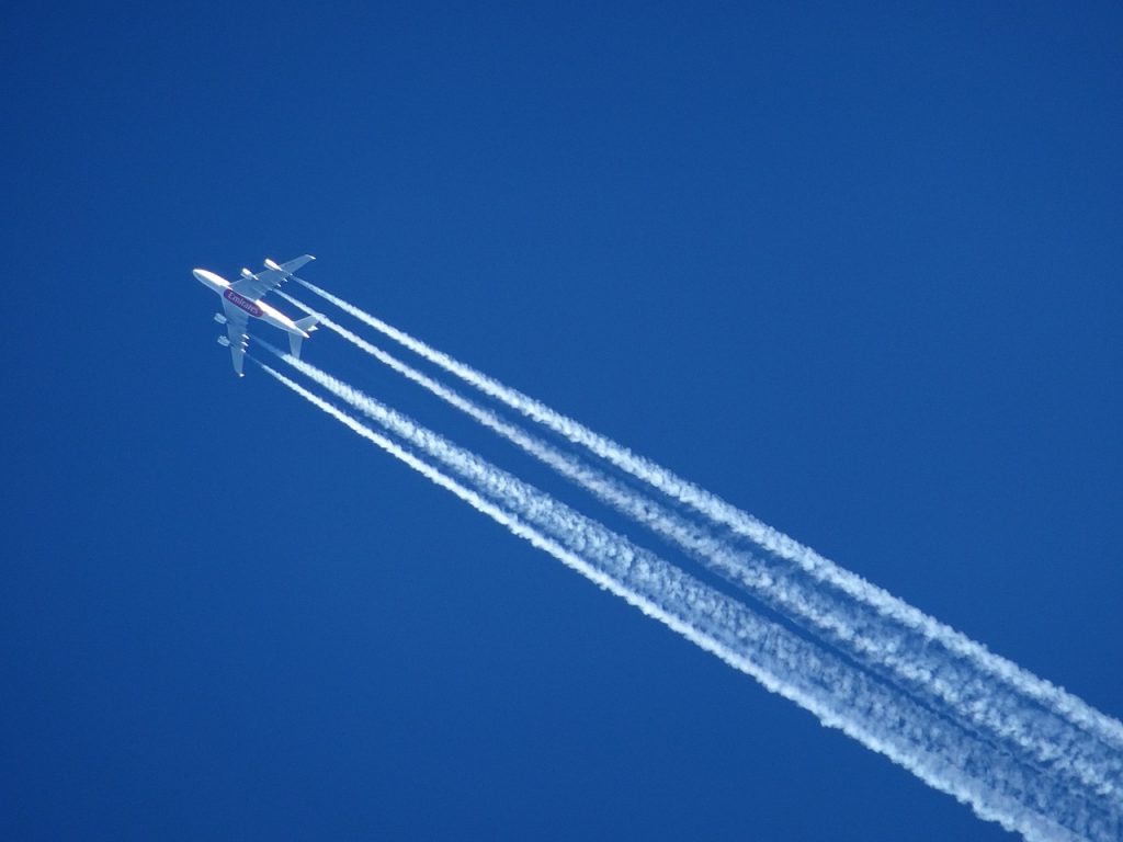 An Emirates aircraft flying and leaving a clear white trail across a blue sky.