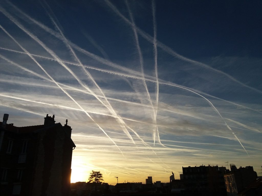 Many plane tracks visible in a clear blue evening sky over a city. 