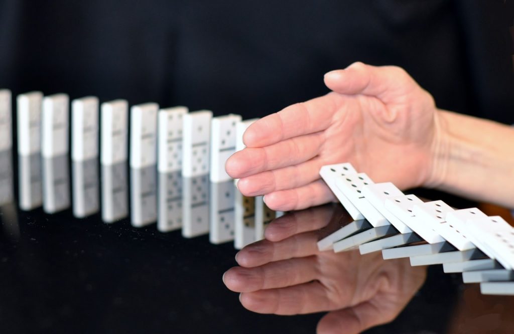 A visualisation of risk management: a hand preventing further collapse in a line of dominoes.