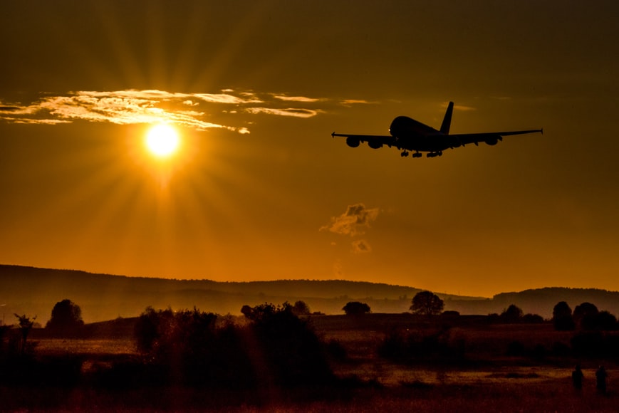 A commercial aircraft takes off in the sunset from an airport in green fields. 