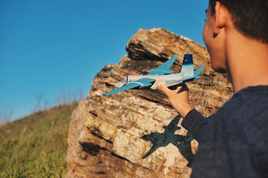 A prototype model of an aircraft being held by a man standing on a green hill. 